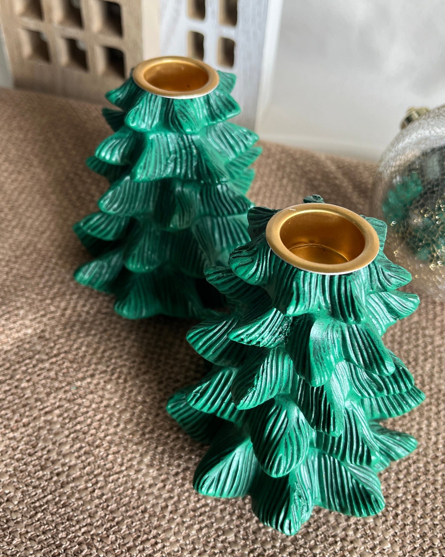 Two green ceramic tree-shaped candle holders with gold bases on a textured surface.