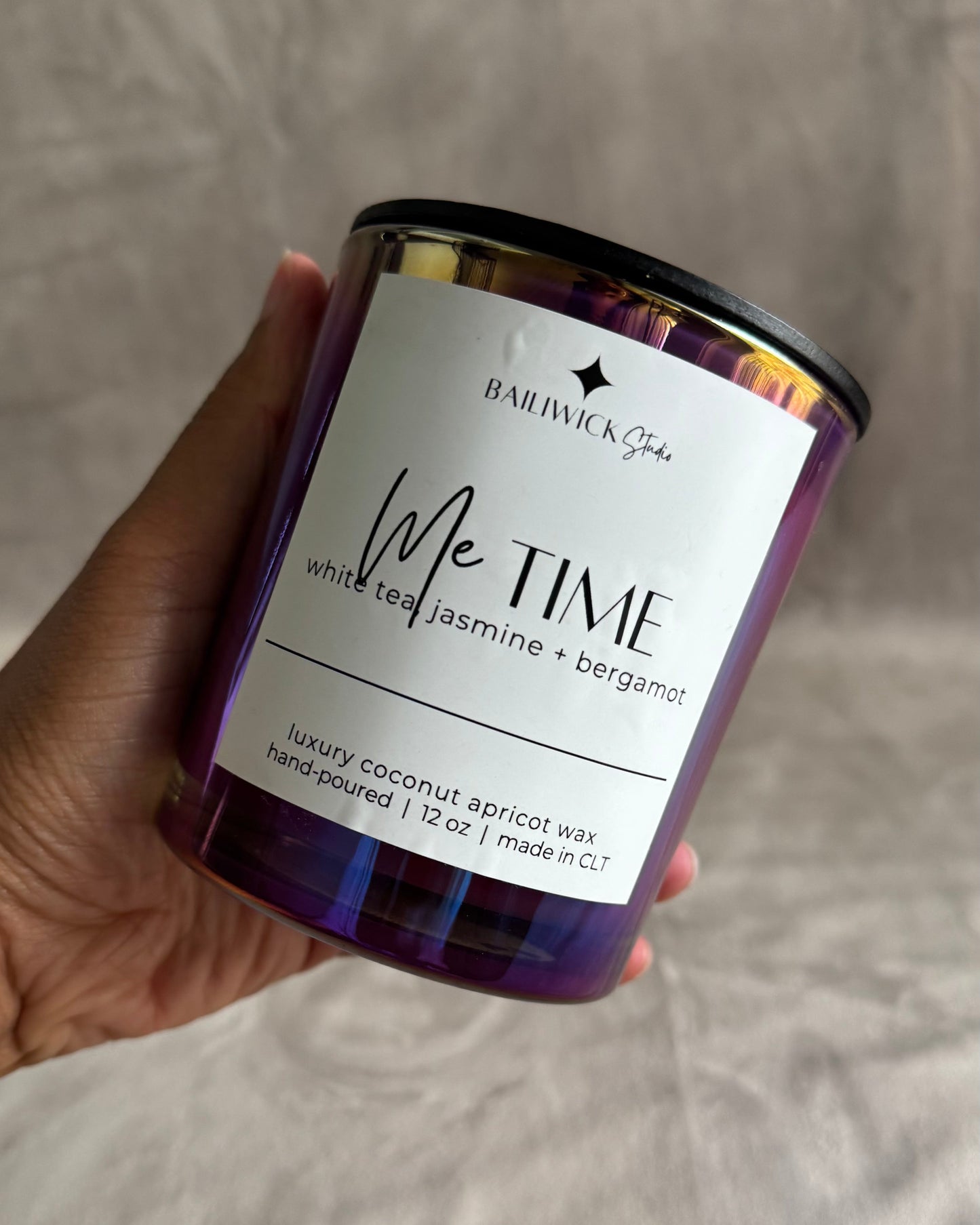 Candle labeled 'Me Time' held by a hand against a neutral background