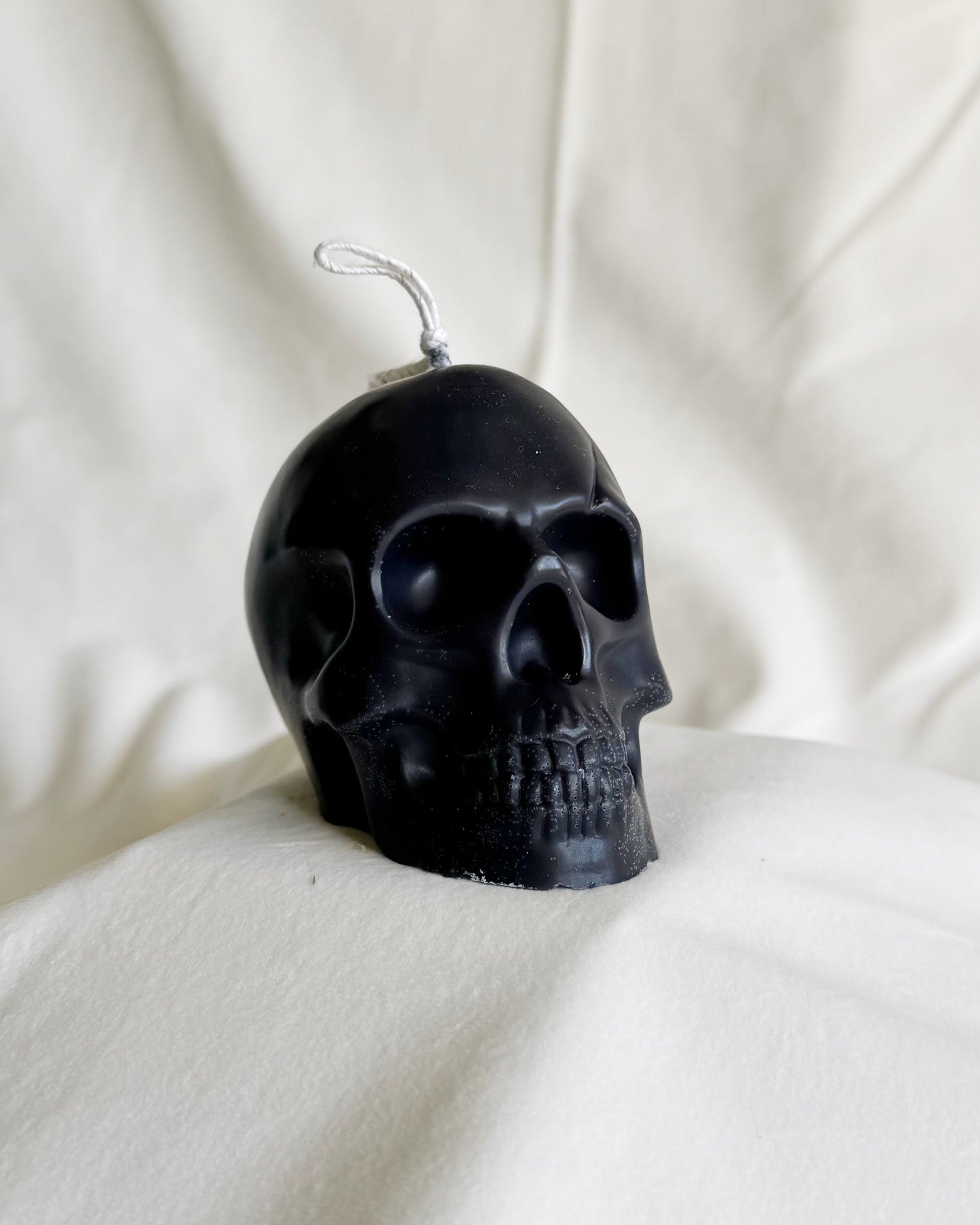 Black skull-shaped candle on a white fabric background