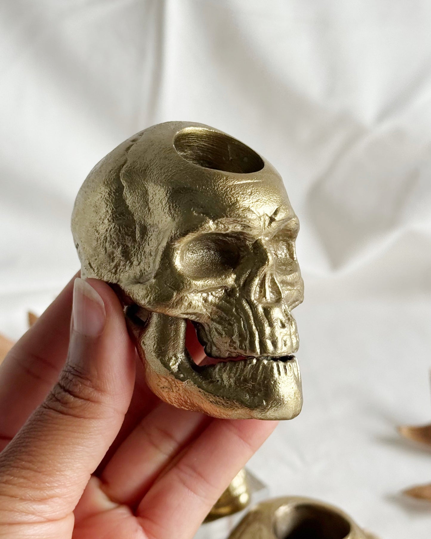Gold skull-shaped object held by a hand against a white background