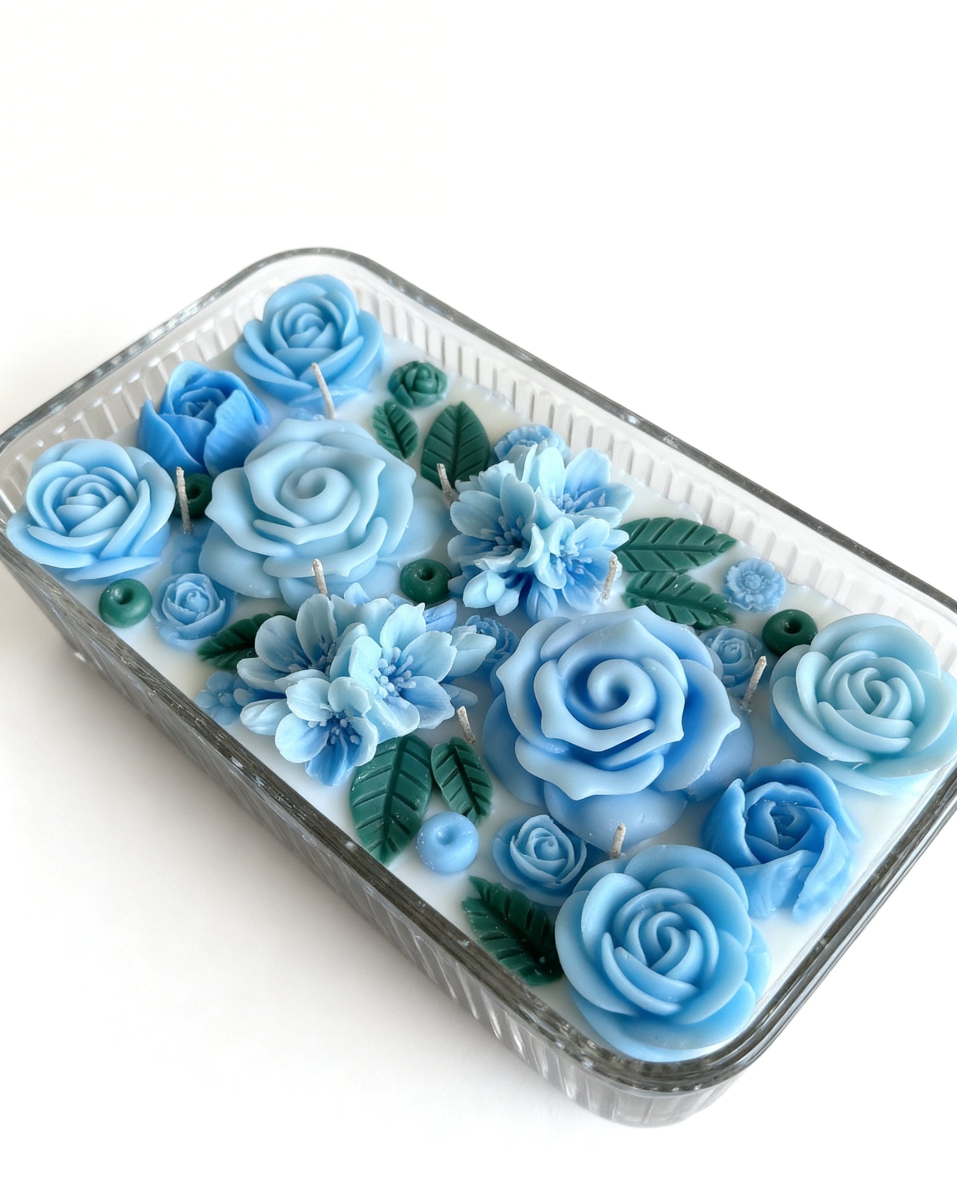 decorative blue candle filled with blue rose-shaped wax roses on a white background