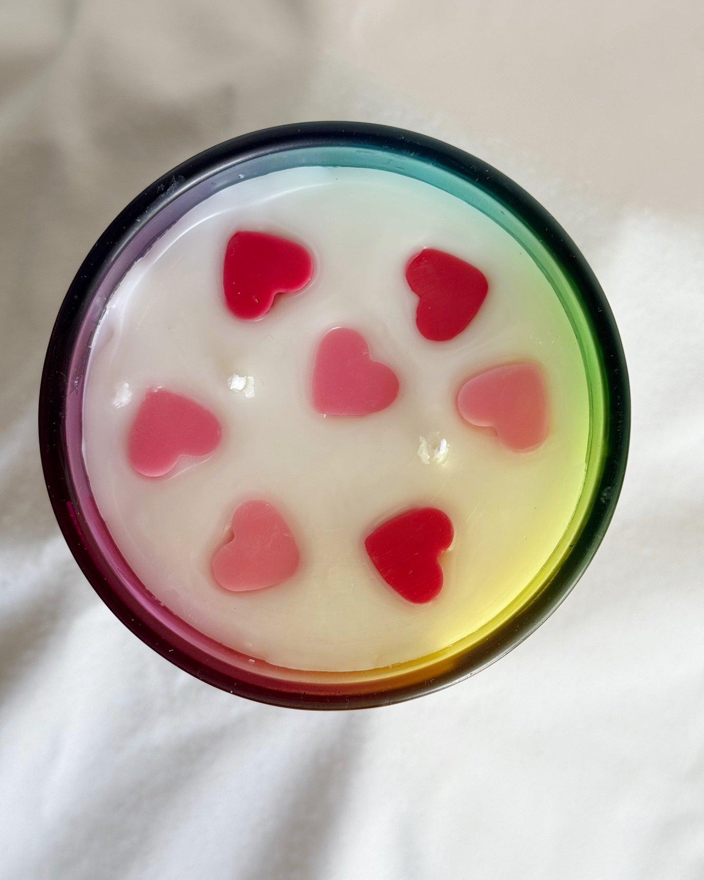 Cup of white liquid with red heart-shaped objects on a light background