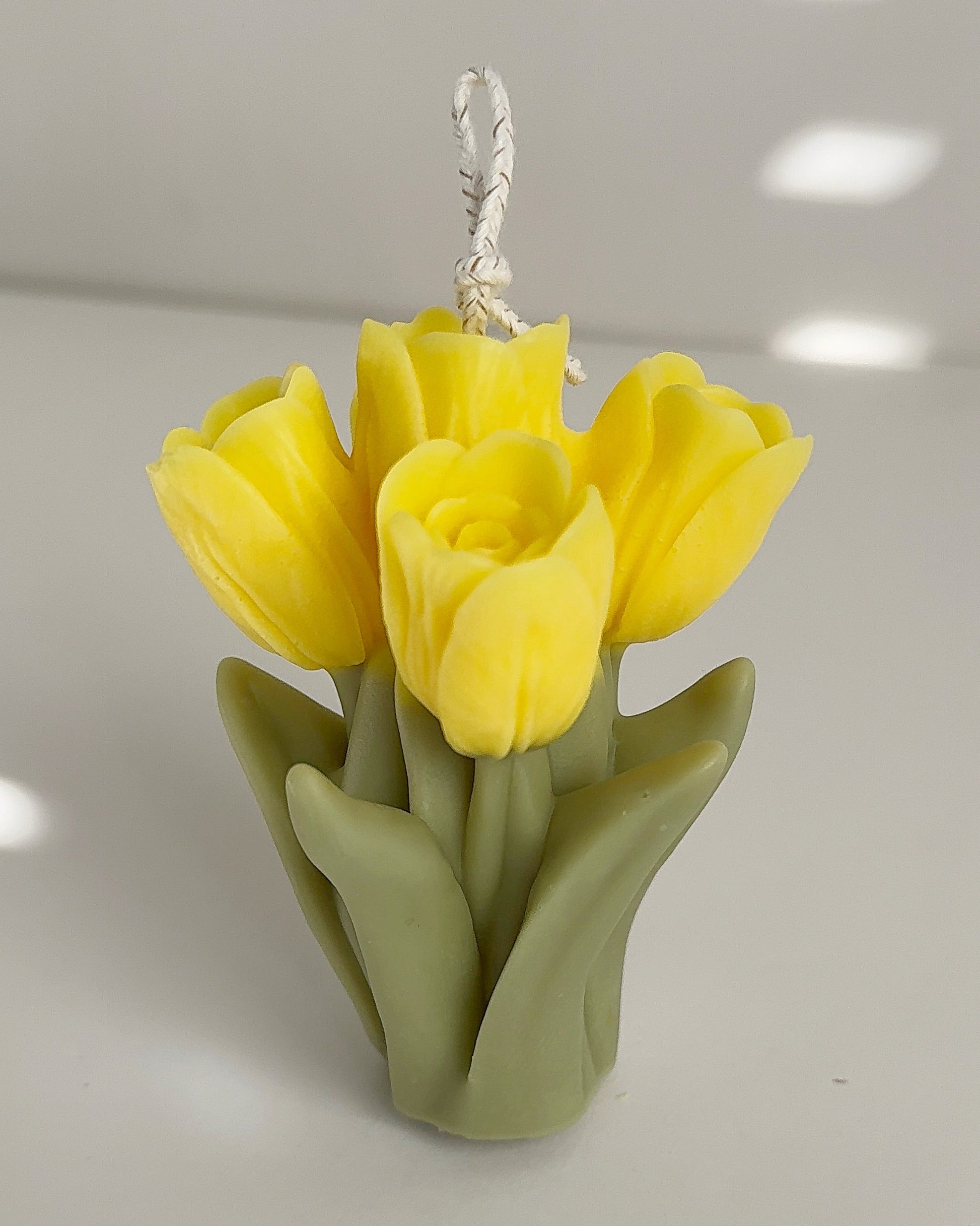 Yellow tulip-shaped candle with a green base on a light gray background