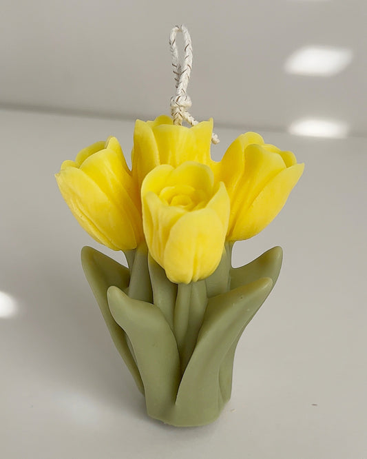 Yellow tulip-shaped candle with a green base on a light gray background