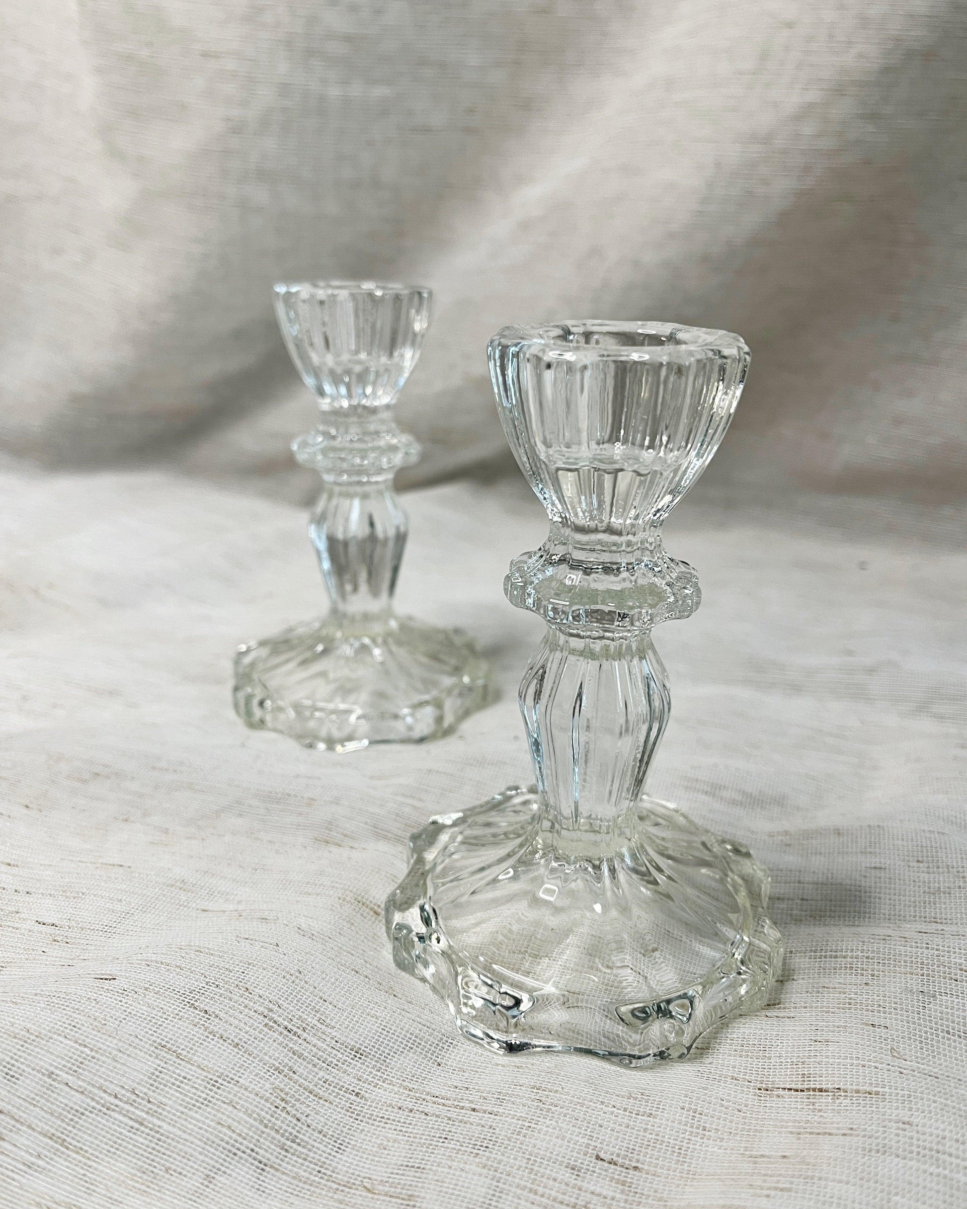 A pair of clear glass candle holders with a tapered design and a small round base, 