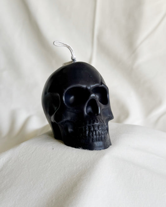 Black skull-shaped candle on a white fabric background