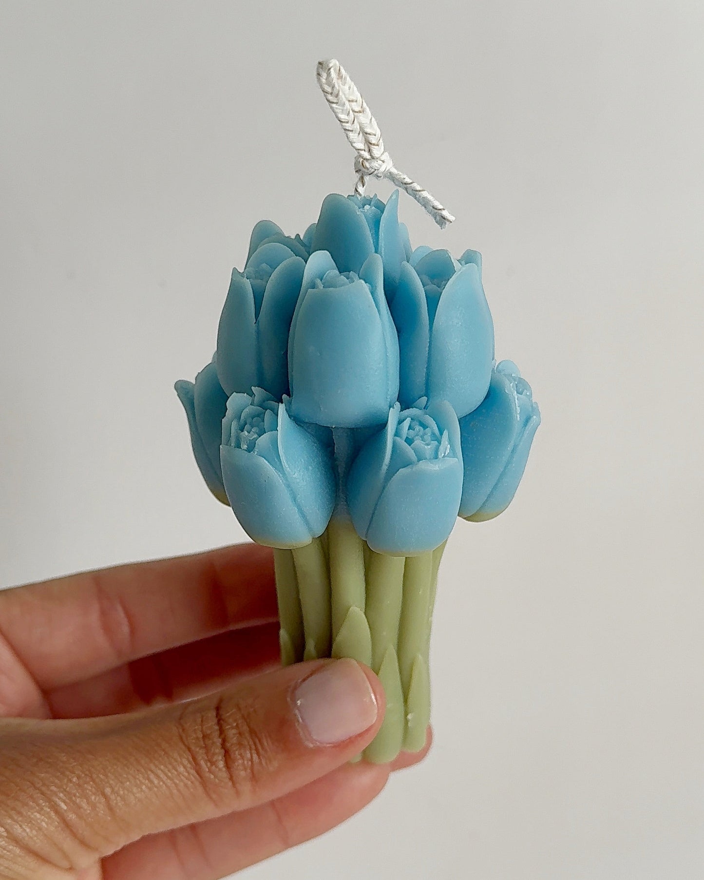 Blue tulip-shaped candles held by a hand against a gray background