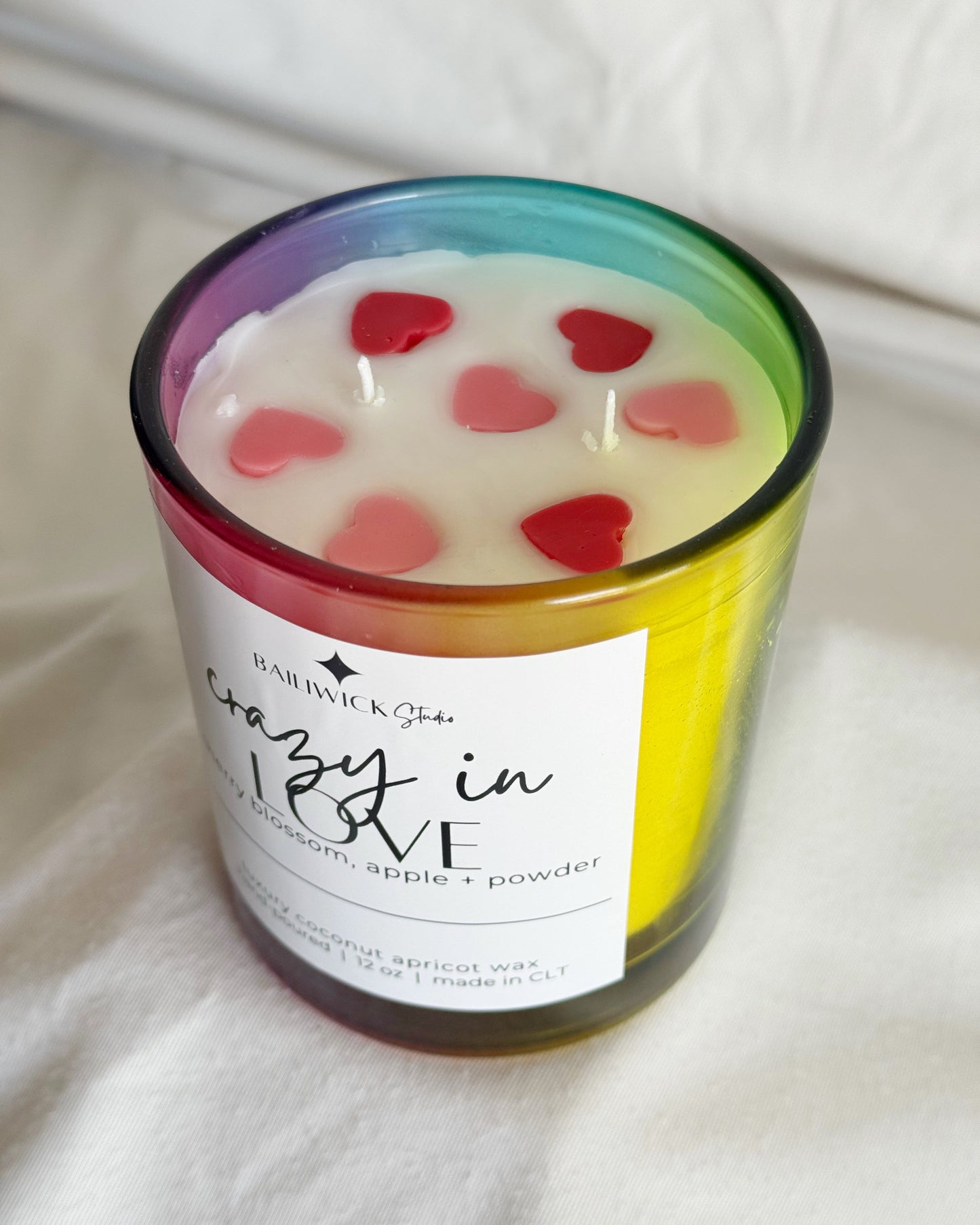 Candle with heart-shaped decorations and a colorful label on a white surface