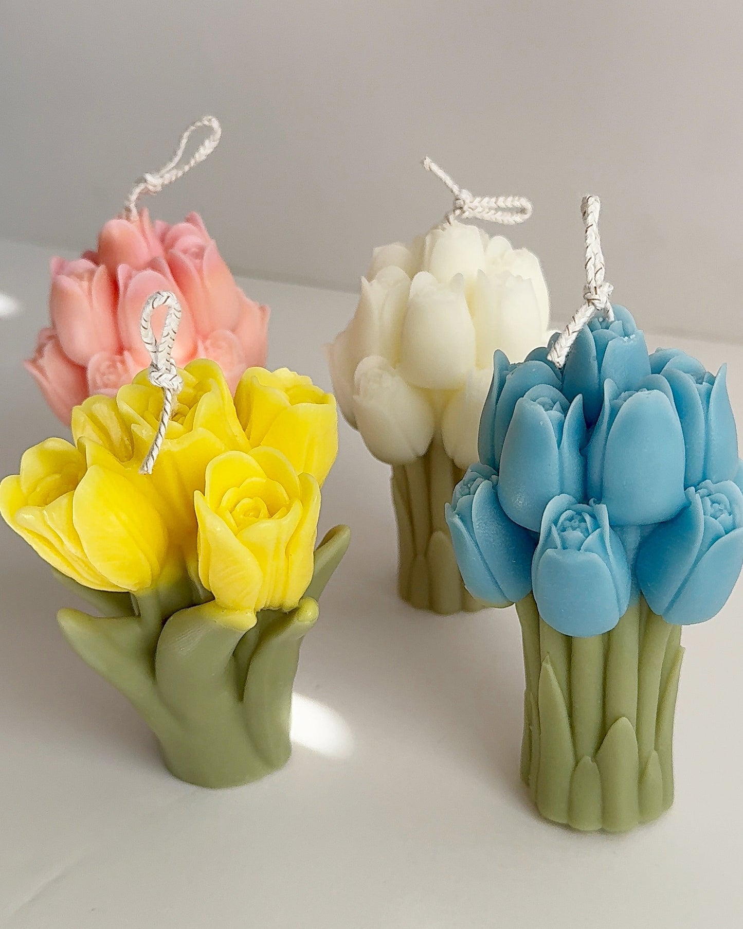 Set of four floral-shaped candles in pink, white, yellow, and blue on a light gray background.