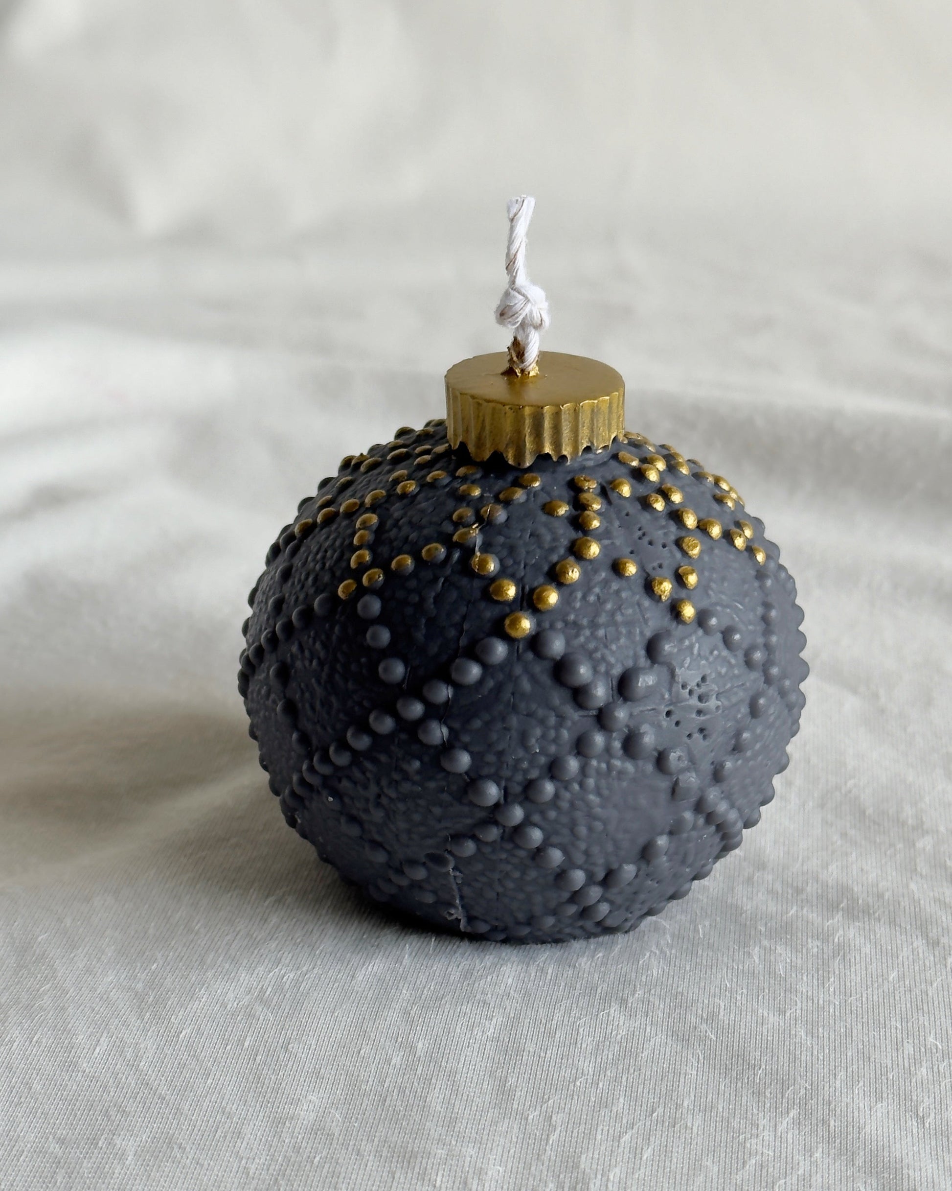 Decorative candle shaped like a textured black ornament with gold accents on a light gray background