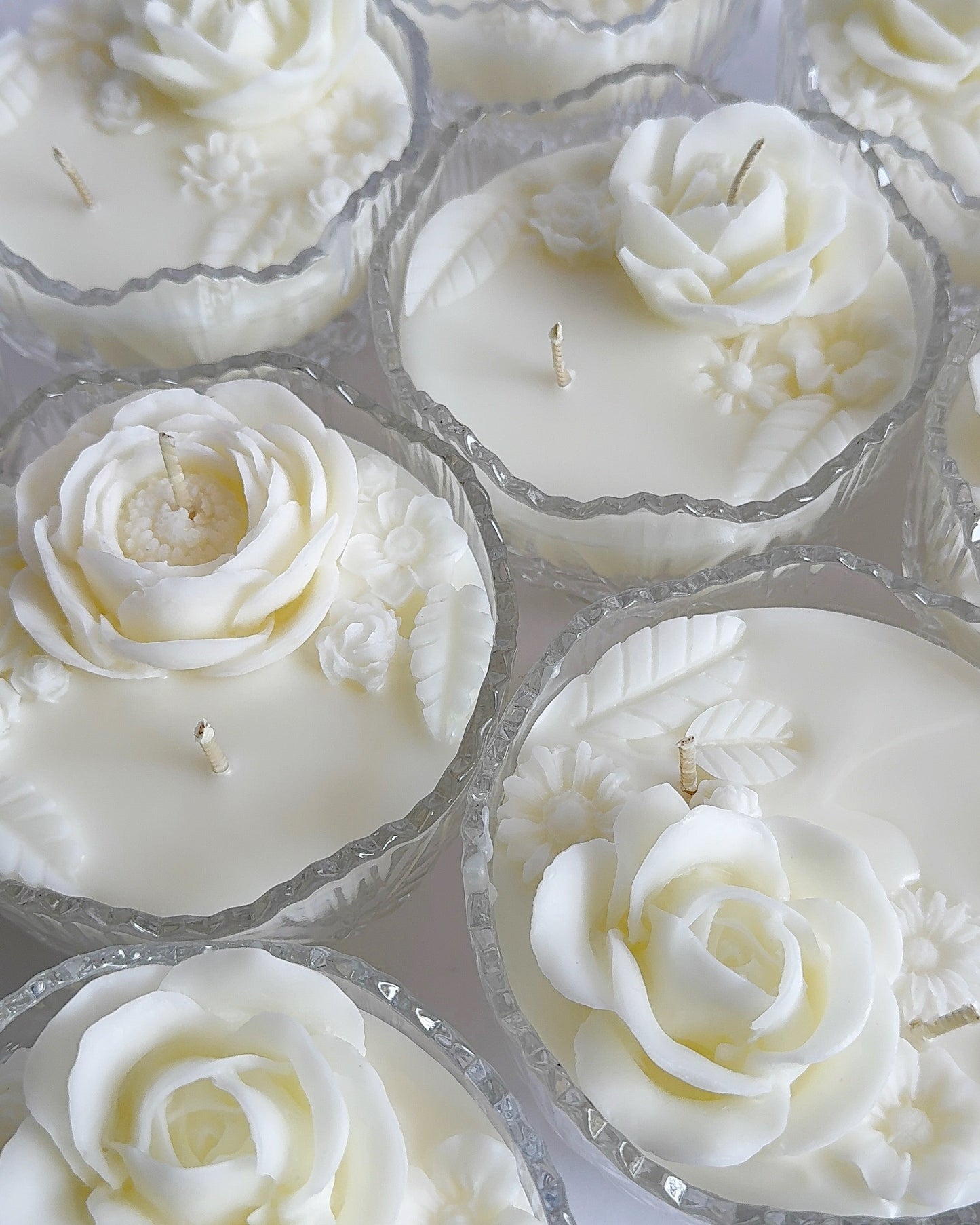 White rose-shaped candles in clear containers on a white background