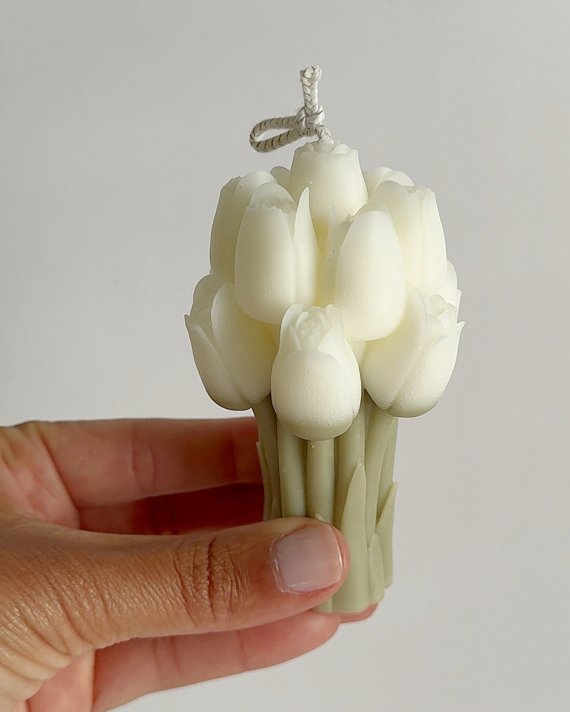 Hand holding a white tulip-shaped candle against a plain background