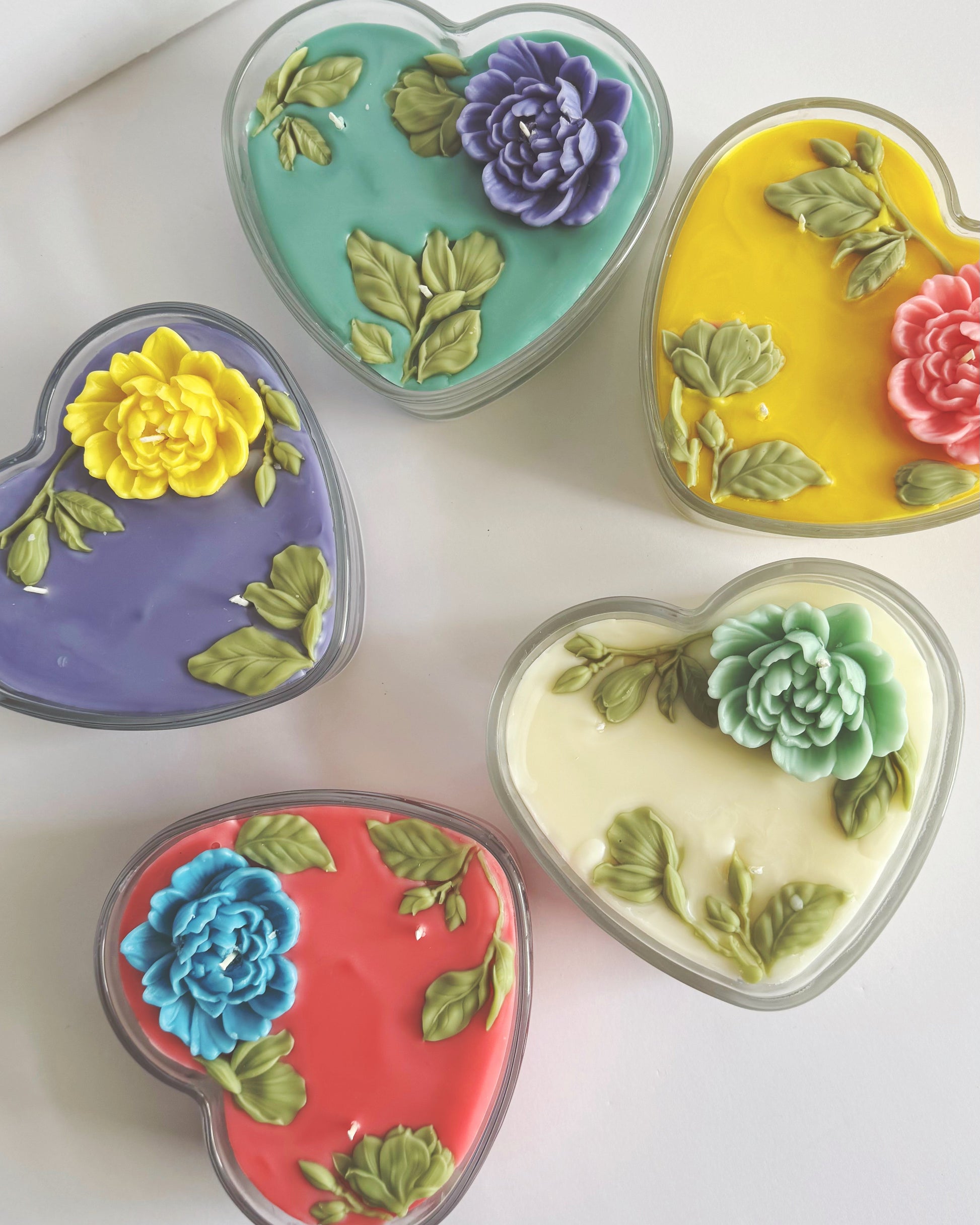 Five heart-shaped candles with floral designs on a white surface