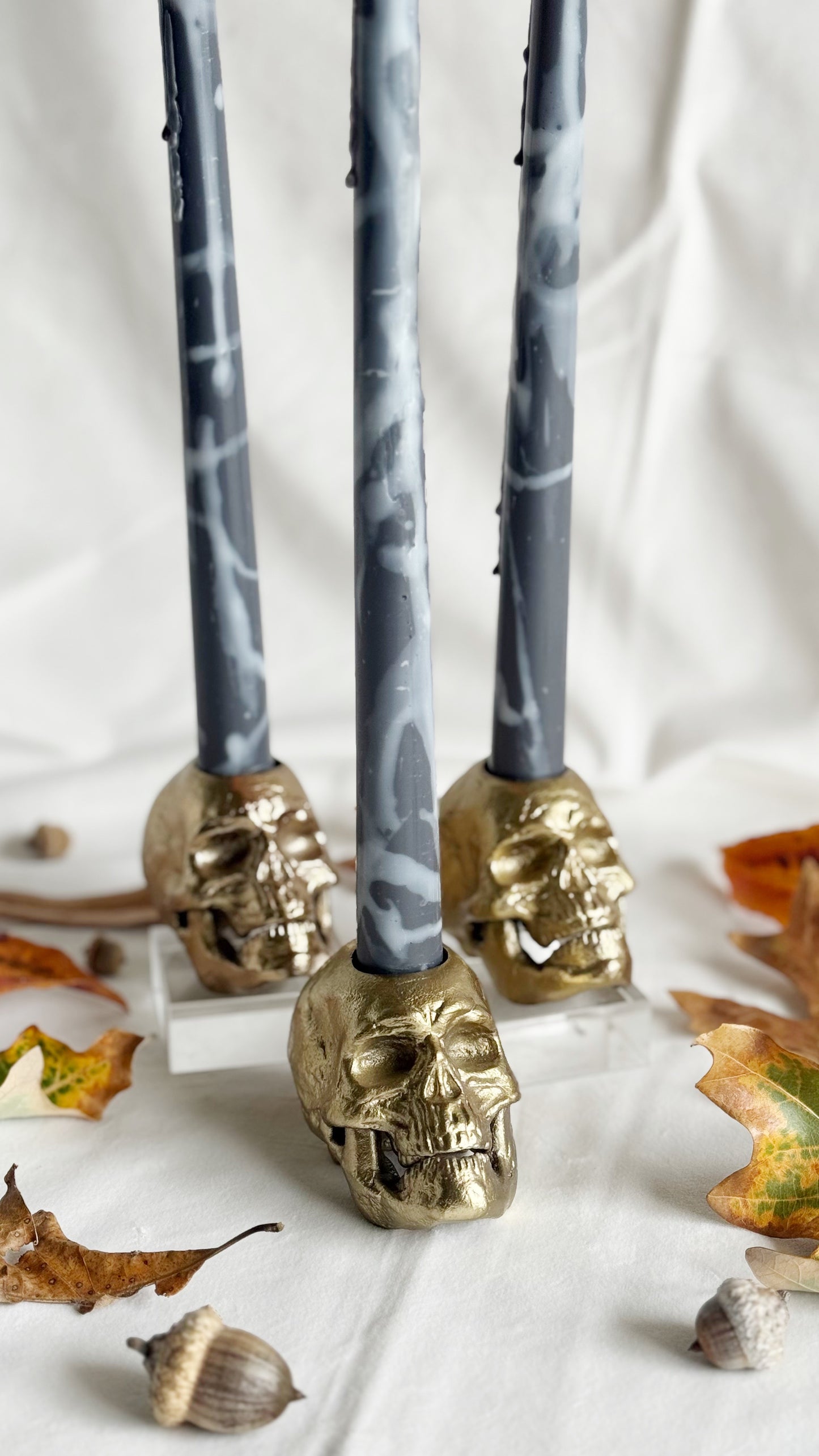 Decorative candles with gold skull holders on a white background with autumn leaves.