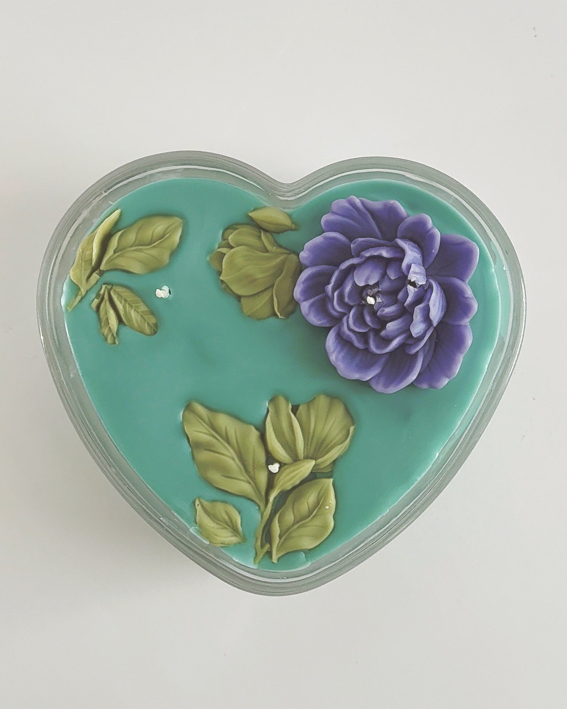 Heart-shaped candle with a purple flower and green leaves on a white background
