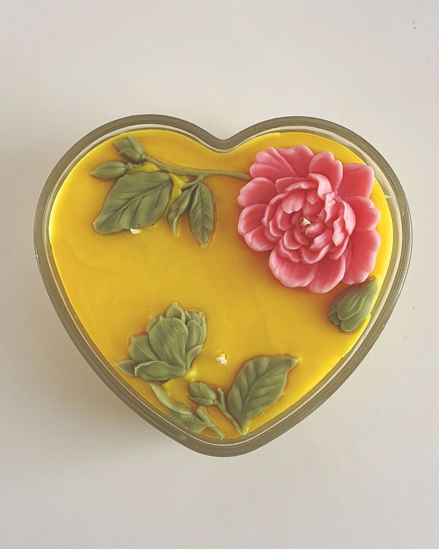 Heart-shaped yellow object with pink flower and green leaves on a white background