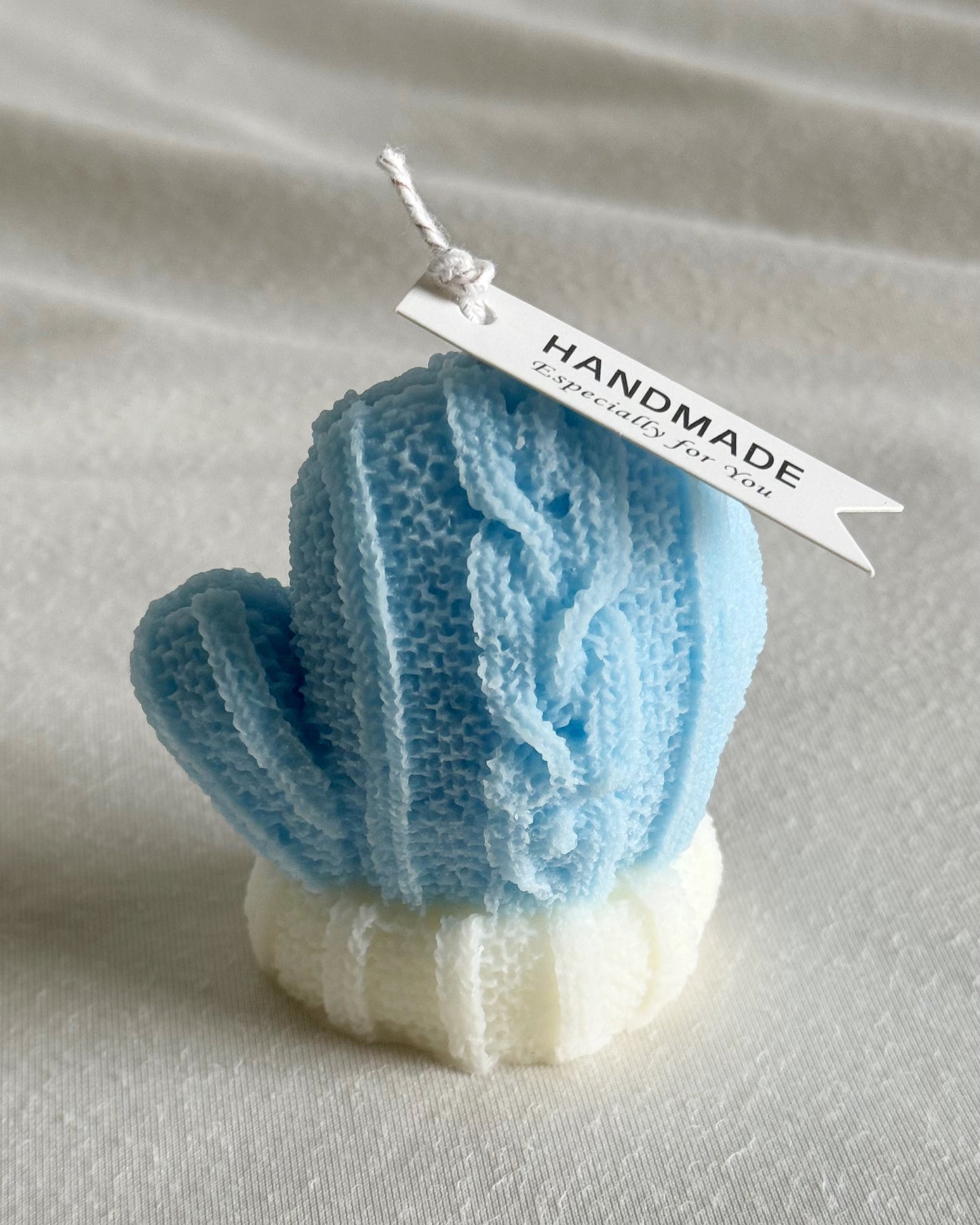 Blue knitted cactus-shaped candle with a 'Handmade' tag on a textured surface