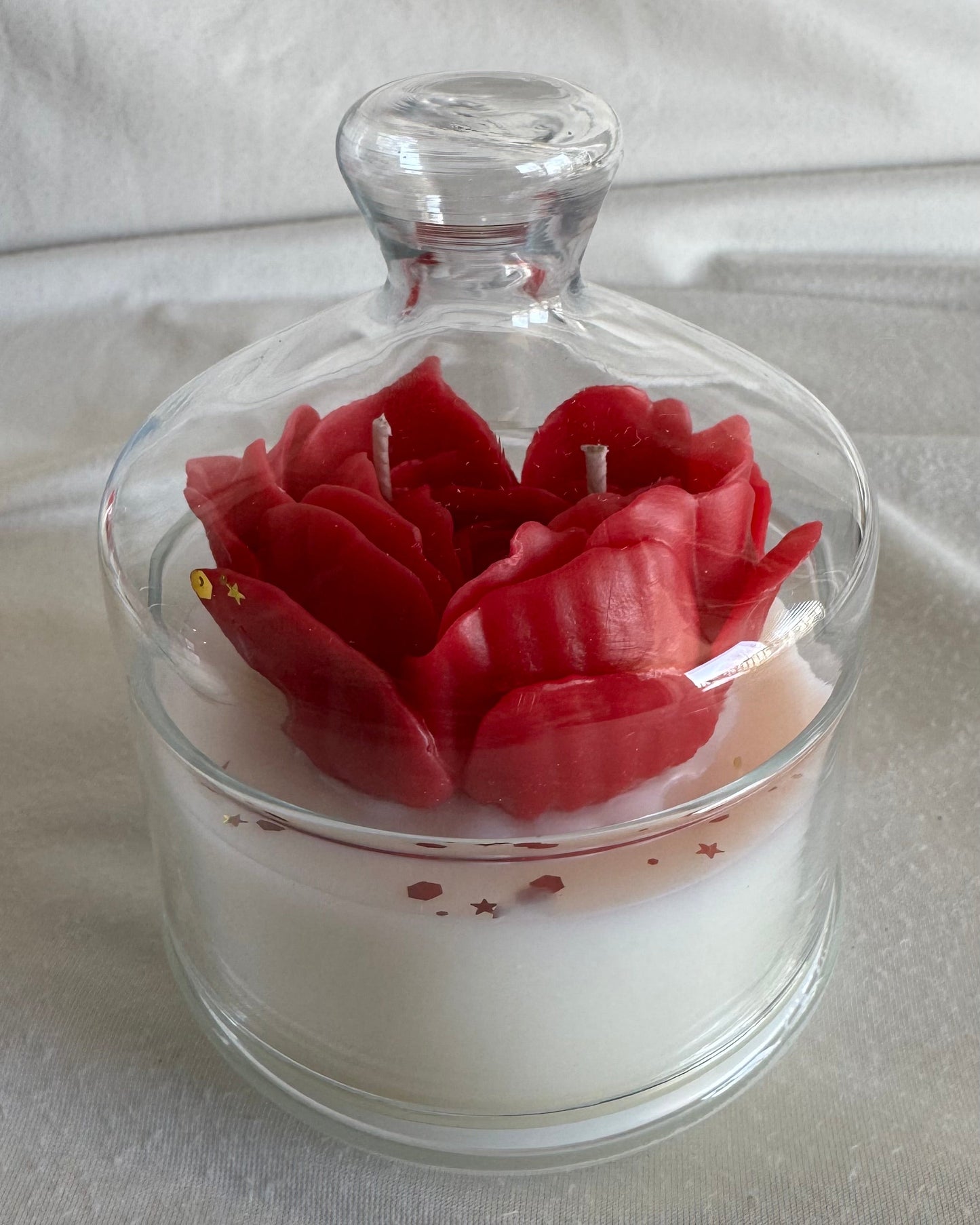 Pink candle shaped like a flower in a glass jar on a white background