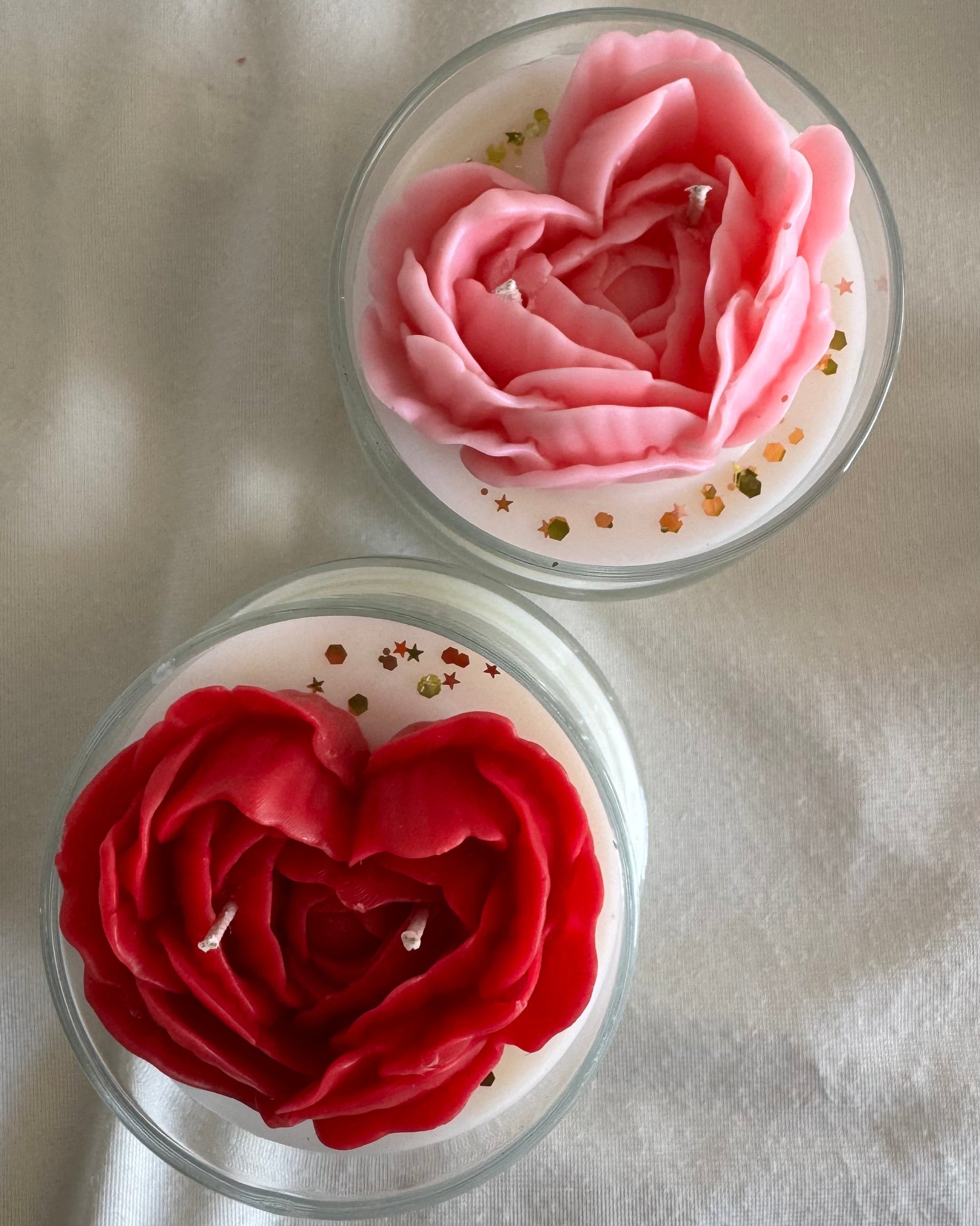 Two small glass containers with pink and red flower-shaped objects on a light gray background