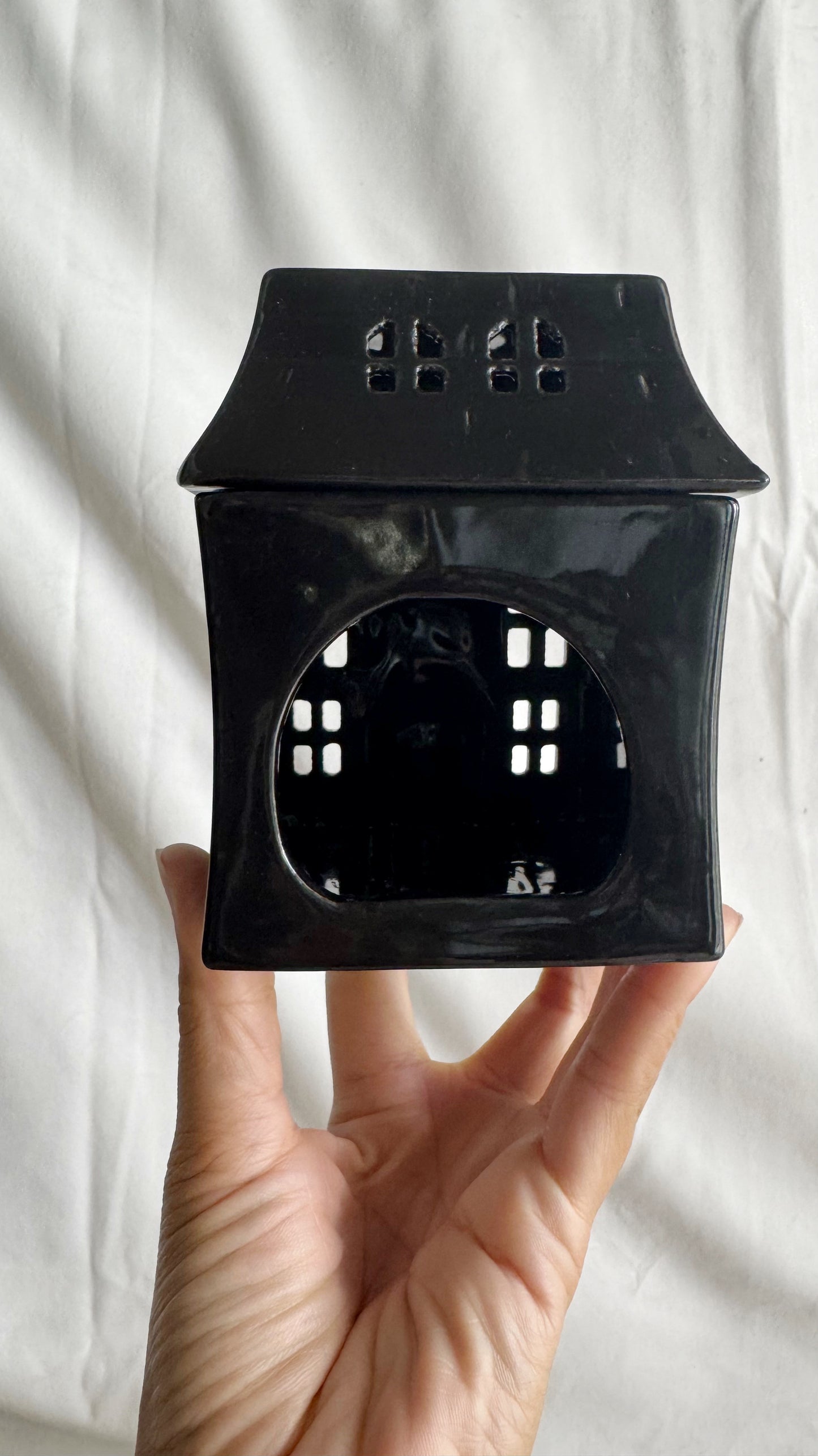 Black ceramic lantern held in a hand against a white background