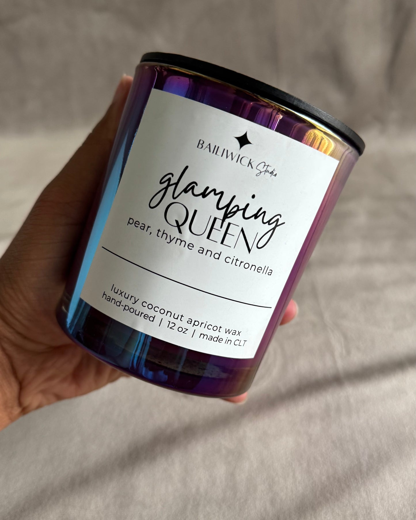 Candle labeled 'Glamping Queen' held by a hand against a neutral background
