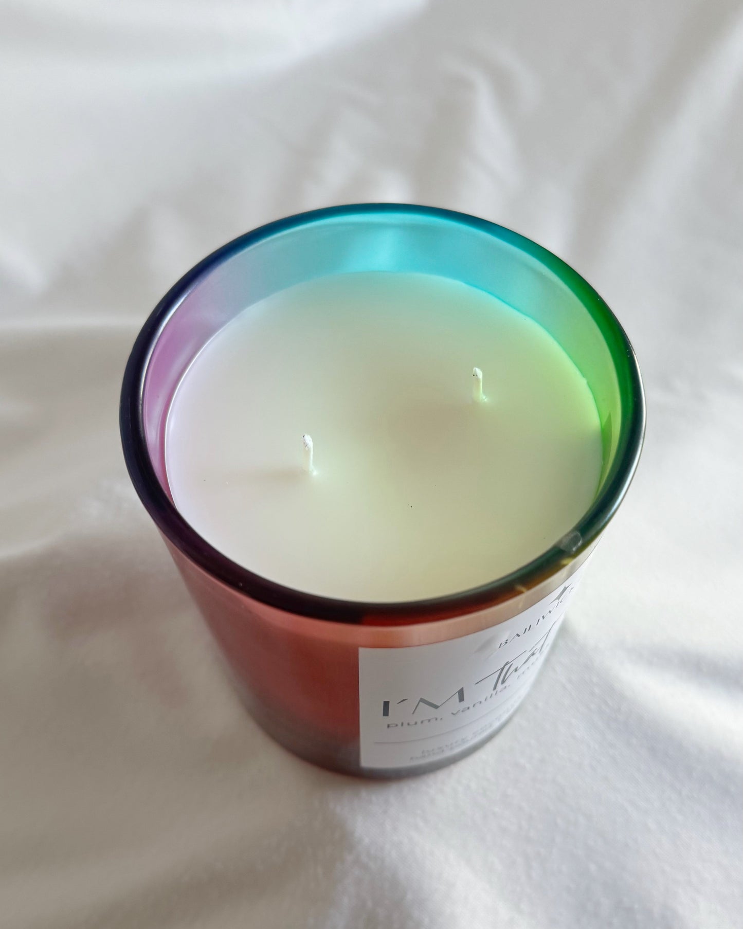 Candle in a rainbow-colored container on a white fabric background