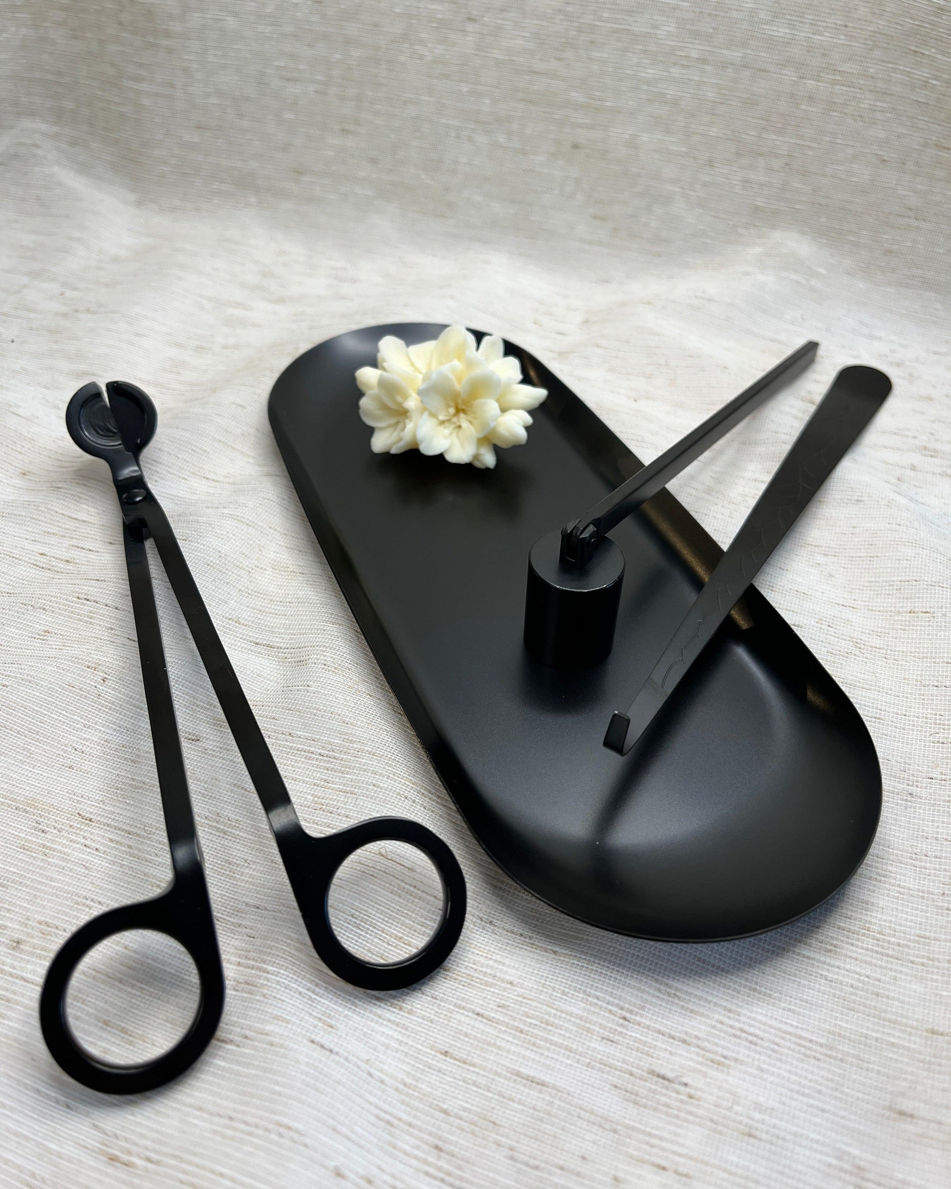 set of black matte candle care tools consisting of a snuff, wick trimmer, and scissors, displayed on a black tray