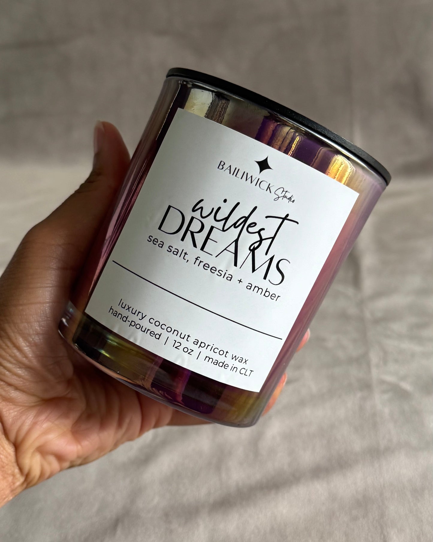 Candle labeled 'Wildest Dreams' held by a hand on a neutral background