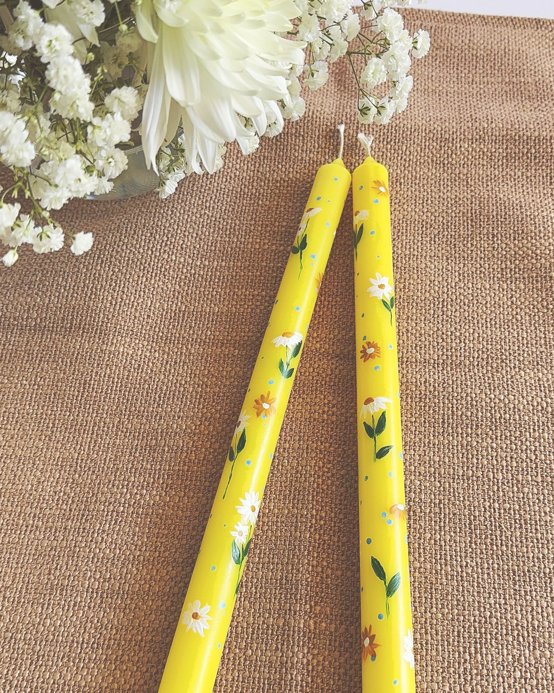 Yellow floral-patterned candles on a textured surface with white flowers in the background