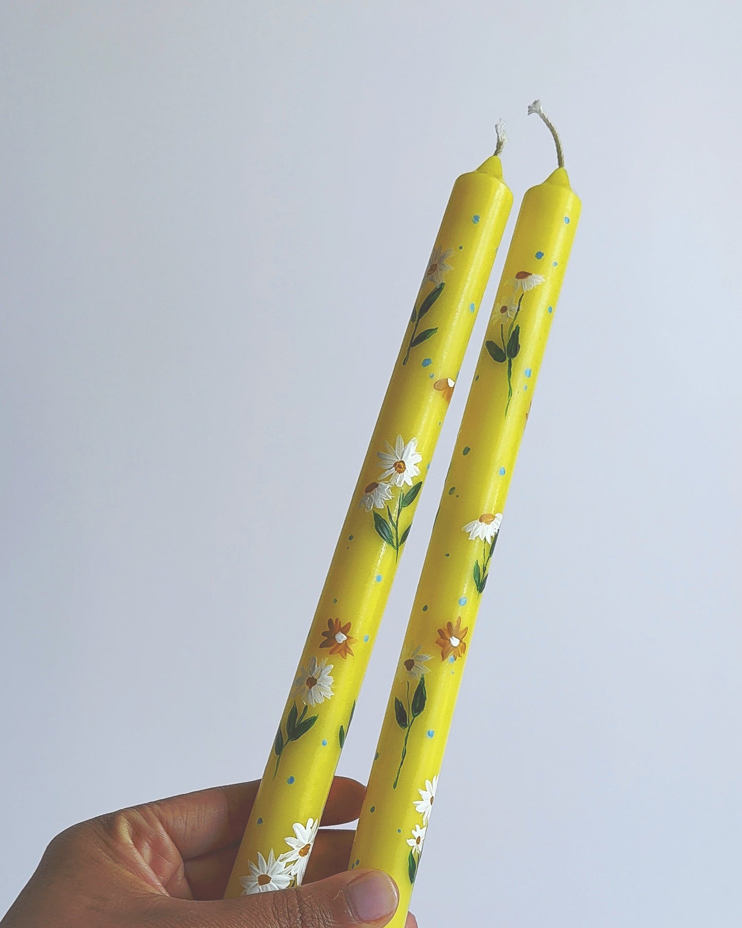 Two yellow candles with floral design held by a hand against a white background